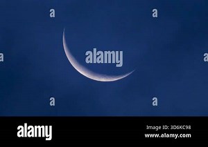 Close up of a thin crescent moon glowing against a deep blue night sky
