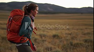 Woman with large orange backpack gazes across dry open landscape