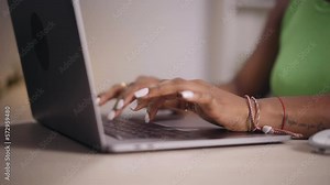 Close up hands of young African woman using laptop in office. Black girl typing on computer and teleworking. People sitting at desk in studio. Concept of enterprising and hardworking person.