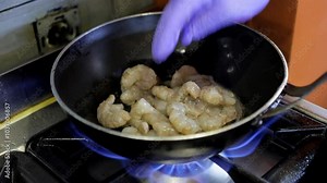 A cook's hands place raw shrimp into a hot wok frying pan in a close-up shot. Seafood preparation and cooking techniques