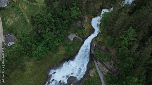 Top-down aerial view of Steinsdalsfossen waterfall in Norheimsund, Norway. Drone footage showing white water cutting through forested terrain and rocky stream below.
