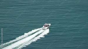Boat Ocean Water Aerial View - A white motorboat moves across the ocean, leaving a wake behind it. The image is taken from an aerial perspective.