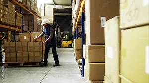 Senior male warehouse worker unloading boxes from a pallet truck.