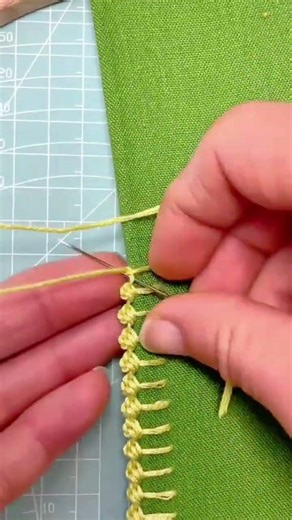 embroidering an intricate yellow pattern with a metal needle and some yellow thread on a green cloth