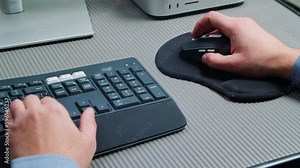 Click computer Mouse on a Work Desk. Working with a PC or laptop. Man Works Behind a Computer in the Office, a Close-up of Hands Holding a Computer Mouse and Keyboard.
