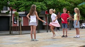 Smiling kids in school age playing together with jumping rope outdoors