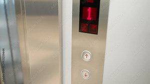 a modern elevator panel with up and down buttons. The scene shows a finger pressing the up button, highlighting the illuminated floor number display and the sleek metallic finish of the panel