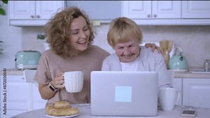 Grandmother talks with adult granddaughter via video call on laptop family love modern technology. Senior grandmother and mid adult granddaughter chat over video call laptop relationships in old age.
