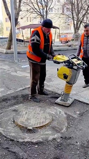 compacting the asphalt around a manhole cover with an electric rammer for a road maintenance work