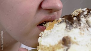 Close up, Face Child Eating a Large Piece of Cake with Cream or a Brownie. Hungry boy opening mouth and bites the pie with teeth. Portrait. Blurred background. Unhealthy foods. Overeating. Birthday