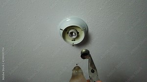 Removing the broken part of a light bulb with a pair of pliers and looking at the broken bulb.