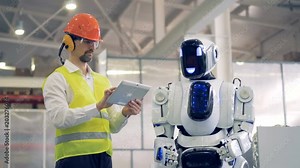 Human-like robot is coming to a factory worker who is showing some gestures to it