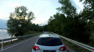 Car riding through road near lake. White SUV driving at dam route on summer day. Follow to auto moving through bridge of river. Scenic landscape way. Concept of trip or journey. Aerial shot Slow mo