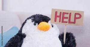 A stuffed penguin toy sitting on the sofa raises a help sign. An excess of low-quality cheap toys. Ecology, minimalism, conscious consumption, parenting. Animal protection, protests.