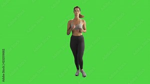 A young woman running in a full body frontal shot over a green screen, looking into the camera and smiles, wearing a sport bra.
