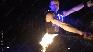 Fire show performance. Handsome male fire performer twirling and tossing up fire baton staff ignited from both sides.