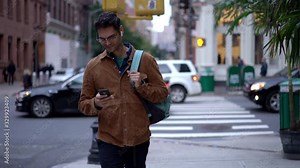 Trendy dressed male blogger in optical eyeglasses walking in downtown and writing content text for sharing to social websites, slow motion of handsome man in earphones listening music records