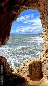 The turbulent Atlantic Ocean with crashing waves viewed from a famous cave at Algar Seco, Carvoeiro, Algarve, Portugal. The scene captures the dramatic interaction between rugged cliffs and the wave