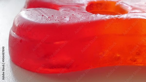 Very close diagonal panning movement of big jelly bear and mixed unfocused jellies behind on white table in studio enviroment at home.