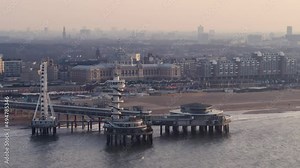 Aerial parallax of the ferris wheel and viewpoint tower on the pier of Scheveningen in Den Haag at sunset