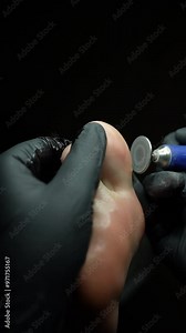 Closeup of professional podiatrist in black gloves giving pedicure treatment to male client, removing hard skin from heel using electric nail file machine. Shooting in slow motion.
