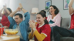 At Home Diverse Group Friends Watching TV Together, Eating Snacks and Drinking Beverage. They Probably Watching Sports Game, Movie or a Sitcom. Young People Having Fun Together.