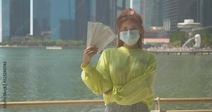 Asian Chinese girl wearing a surgical face mask and holding extra face masks in her hands to protect herself from COVID-19 coronavirus infection in crowded public places