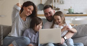 Happy family of four parents mum dad and little kids children enjoy using laptop having fun together watching cartoons online make video call internet shopping looking at computer sit on sofa at home