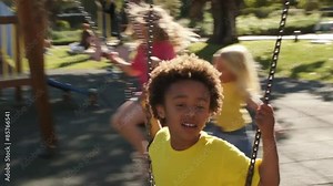 Slow motion of four children playing on swings in park.