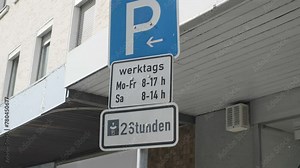 Footage of a blue "parking" sign on a metallic pillar on the street