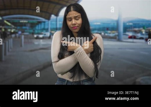 Woman arms crossed with fingers pointing in opposite directions at airport entrance with cars behind; uncertainty Stock Video Footage - Alamy