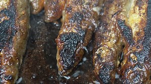 View of cooking frying capelin fish in iron pan. Grilled caplin fish - nutritious traditional unhealthy Asian dish