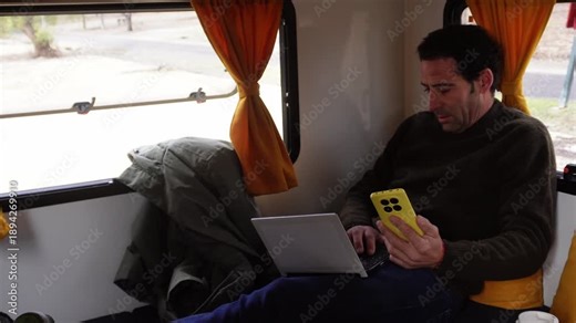 Man multitasking on his laptop and smartphone while sitting inside a campervan. Digital nomad living the van life and working on the go