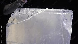 Ice sculpture creation process, artist is breaking off pieces of ice with chisel