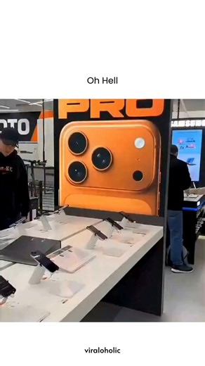 VIRAL VIDEOS on Instagram: "This video captures a clever and humorous 16-second prank set inside a busy electronics retail store. The footage begins by panning across a display of iPhones, only to reveal that a young man has set his own selfie as the lock screen wallpaper on one of the demo units. The camera then reveals the punchline: the same man is standing just a few feet away at the display table, casually browsing while wearing the exact same black "NIKE" hoodie and baseball cap seen in th