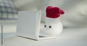 Snowball with eyes and Santa hat using laptop, notebook. Funny, interesting concept of snow winter character with face and living eyes watching, blinking. Winter, Christmas online concept.