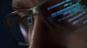 Extreme close-up of a programmers eye with computer code reflecting on glasses, symbolizing cybersecurity, coding, and software development.