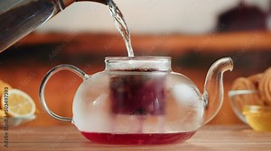 Brewing red tea close-up. Pouring hot water into teapot with fruit tea on a wooden table. Freshly brewed hibiscus tea ceremony process, healthy morning, detox drink.