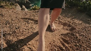 Barefoot woman gracefully dancing on sandy ground, performing a modern dance with feet making circles.