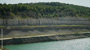 Multi-layered limestone rocks rise above clear blue lake. Concept of natural minerals.