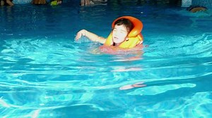A child in an orange life jacket swims in the pool in an aqua complex for family holidays. Safety on the water, learning to swim