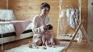 Eco-Conscious Parenting: A cheerful mom swaps clothes for her baby girl, emphasizing sustainable wooden toys scattered around their wooden home