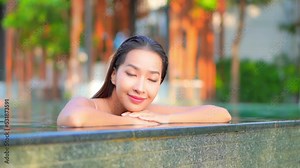 Close-up of a pretty young woman leaning along the edge of an infinity pool as water drips over the edge.