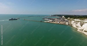 Aerial view of port of Dover with a ship entering harbour, busy car and passenger ferry terminal, and picturesque white cliffs, countryside fields, south east England, Kent, on a sunny summer day .