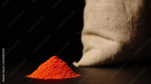STOP-MOTION: Red pepper powder heap growing near a cloth sac on a black background