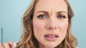 A serious woman is looking to the peephole standing isolated over blue wall in a studio