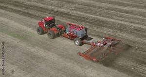 Field works. Tractor sowing seeds with seeder driller in field. Process of sowing cereals and other crops. Sowing work in the field. Tractor with seeder performing seeding. Top down drone view.