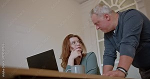 In a modern office environment, cross-generational business employees engage in a discussion over a laptop, exchanging ideas and strategies, showcasing the diversity and collaboration within the team.