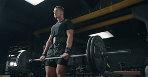 Focused male athlete performing heavy deadlifts in an industrial-style gym, showcasing fitness and determination. Dedicated Young Man Performing Deadlifts at Modern Gym