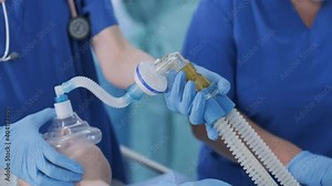 The anesthesiologist in medical gloves prepares female patient for surgery, puts patient into anesthesia, regulates oxygen mask. The nurse administers intravenous catheter. Surgery. Anesthesia